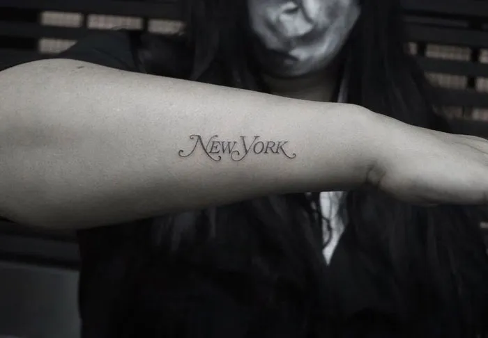 "Word tattoo 'New York' on a forearm, in elegant script."