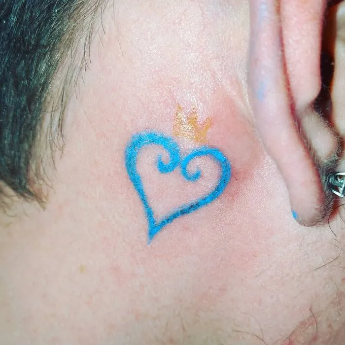 Blue heart ear tattoo with a small golden crown above it.