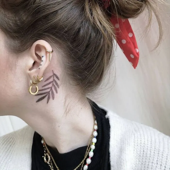 Leaf design ear tattoo with piercings, red polka dot hair tie, showcasing unique ear tattoo ideas.