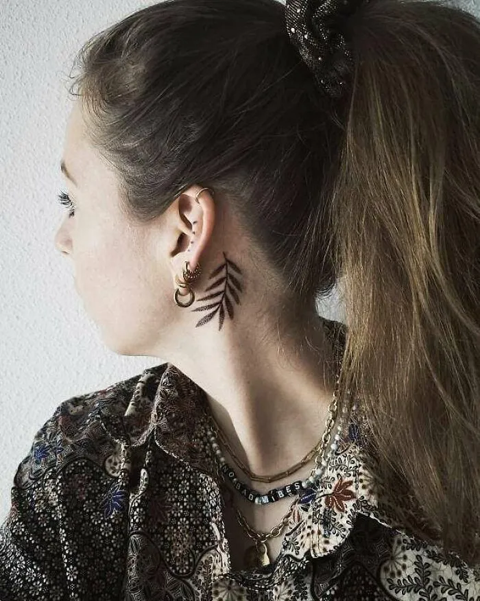 Woman with leaf ear tattoo, wearing patterned shirt and gold earrings, showcasing unique tattoo style.