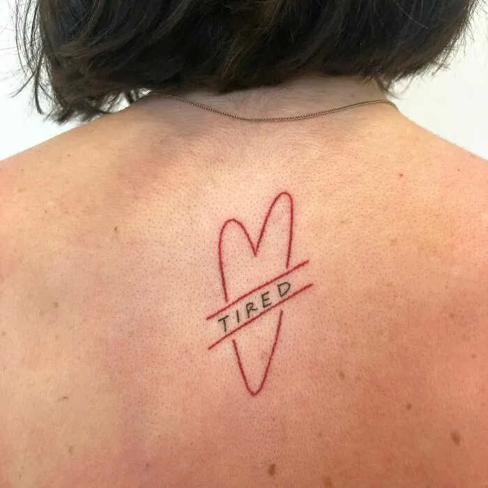 Heart-shaped tattoo with the word "tired" on skin, showcasing creative word tattoos for inspiration.