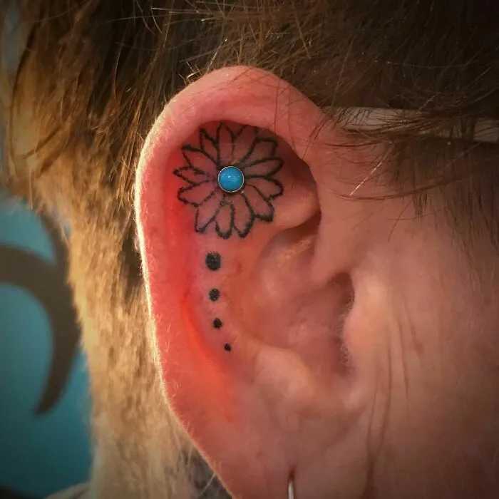 Ear with a flower tattoo and blue stud, showcasing subtle ear tattoo design.