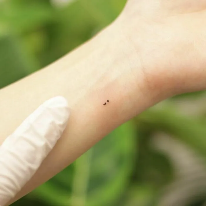 Minimalist tattoo of a tiny semicolon design on a wrist, emphasizing simplicity and style.