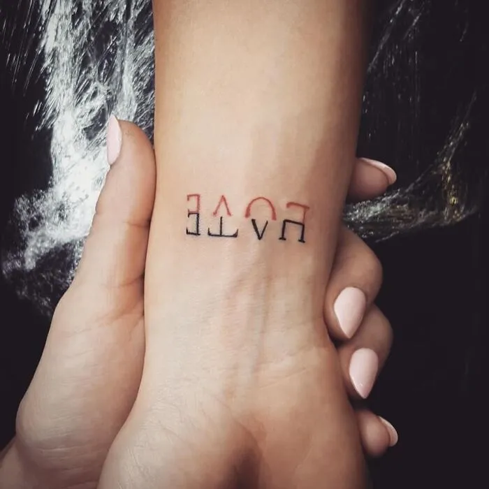 Upside-down "LOVE" tattoo on a wrist, held gently by a hand.