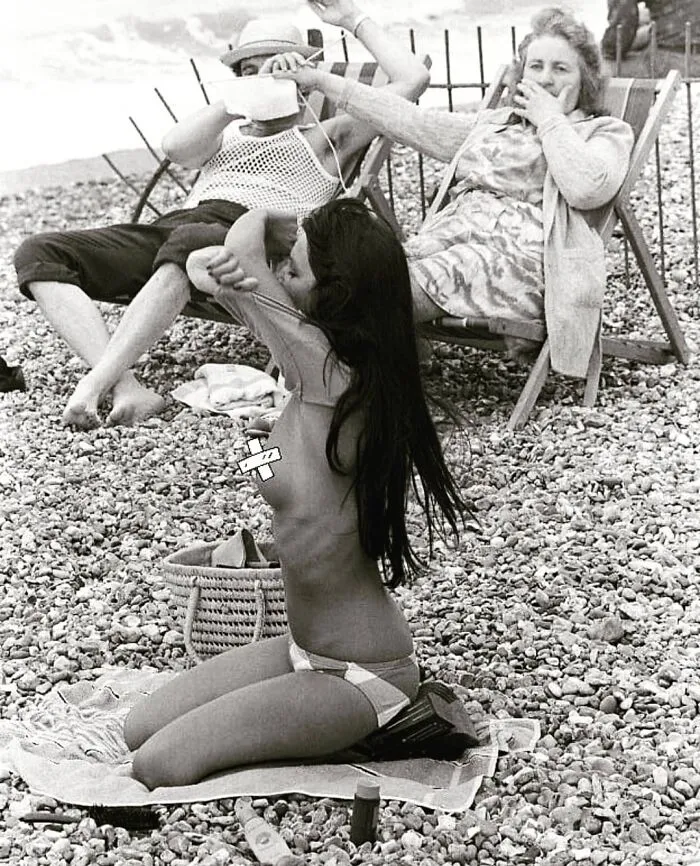 Old couple in a beach looing at a woman who is taking her top of 