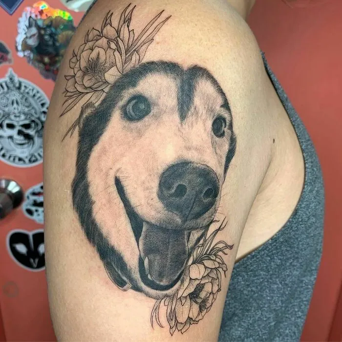 Pet tattoo of a dog's face with floral accents on a person's upper arm.