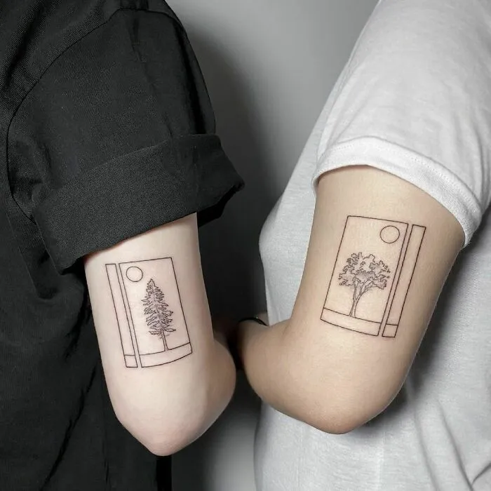 Matching tree tattoos on arms symbolize friendship and connection for best friends.