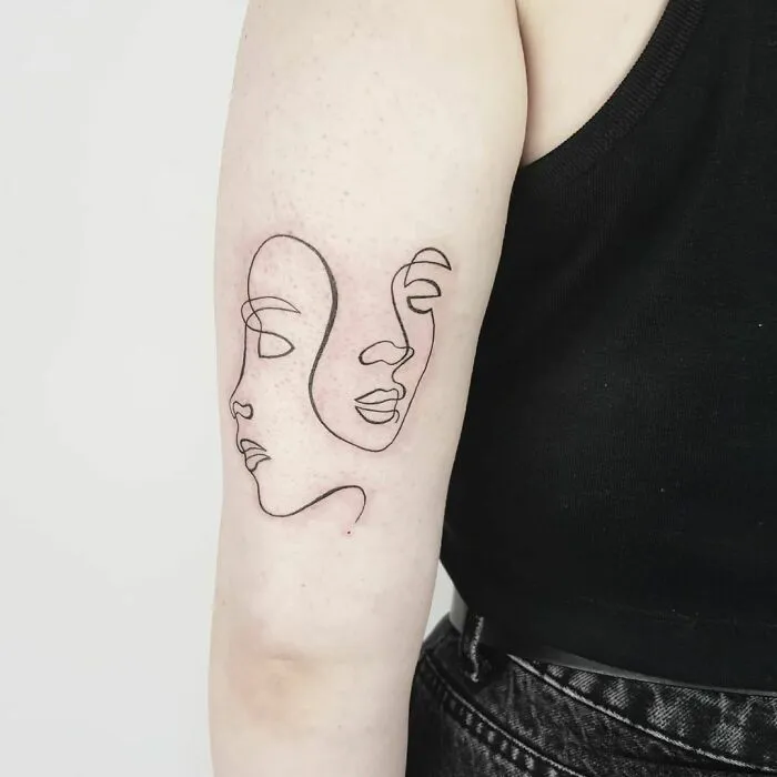 Fine-line tattoo of two abstract faces in single-line style on upper arm.