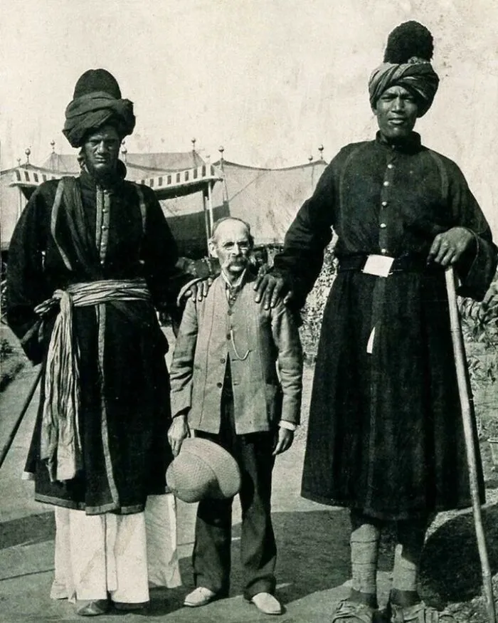 Two super tall men posing near a small American man 