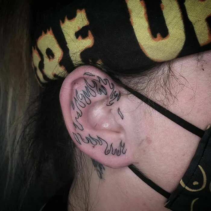 Black flame design ear tattoo on a person's ear, showcasing creative tattoo art style.