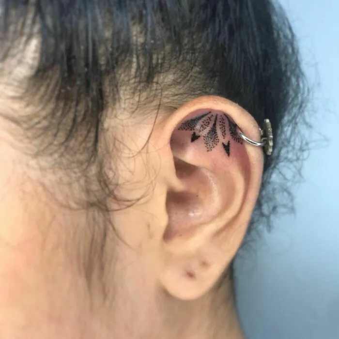 Intricate ear tattoo with decorative black patterns and a hoop piercing.