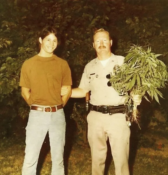Man arrested by a police officer who is holding a marijuana plant in his hands 