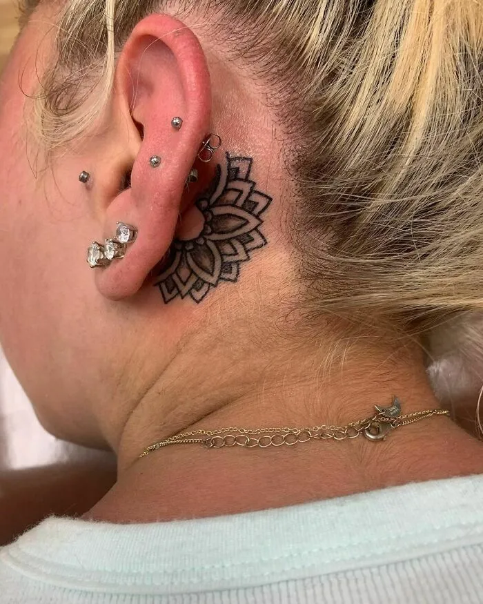 Floral ear tattoo with multiple piercings and a gold necklace on a blonde-haired person.