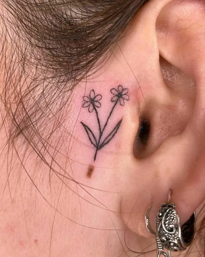 Delicate flower ear tattoo design showcasing subtle ink placement behind the ear.