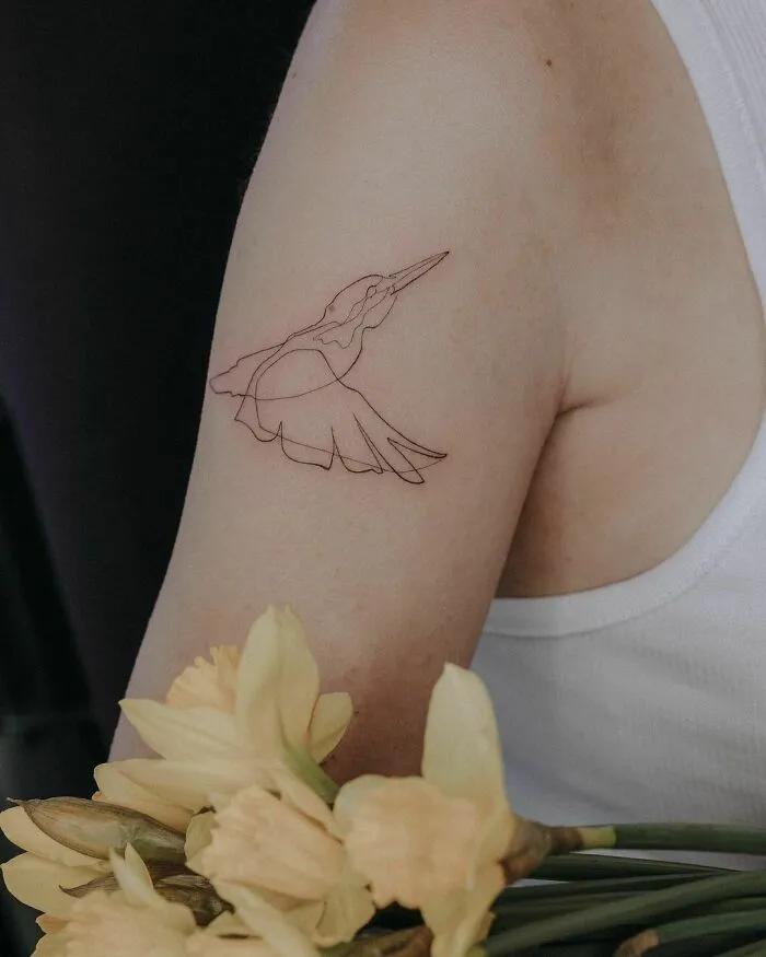 Single-line fine-line tattoo of a bird on an arm, accompanied by a bouquet of yellow flowers.