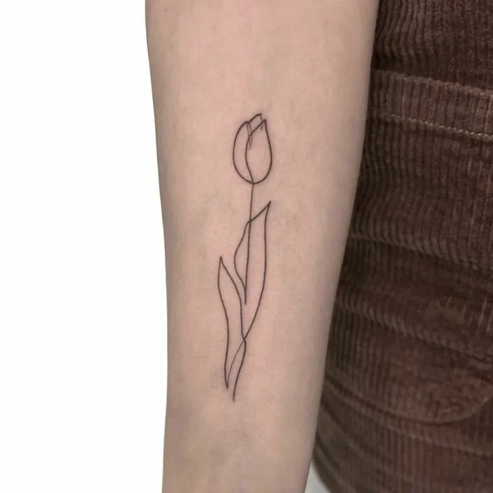 Single-line tattoo of a tulip on forearm, showcasing fine-line perfection.