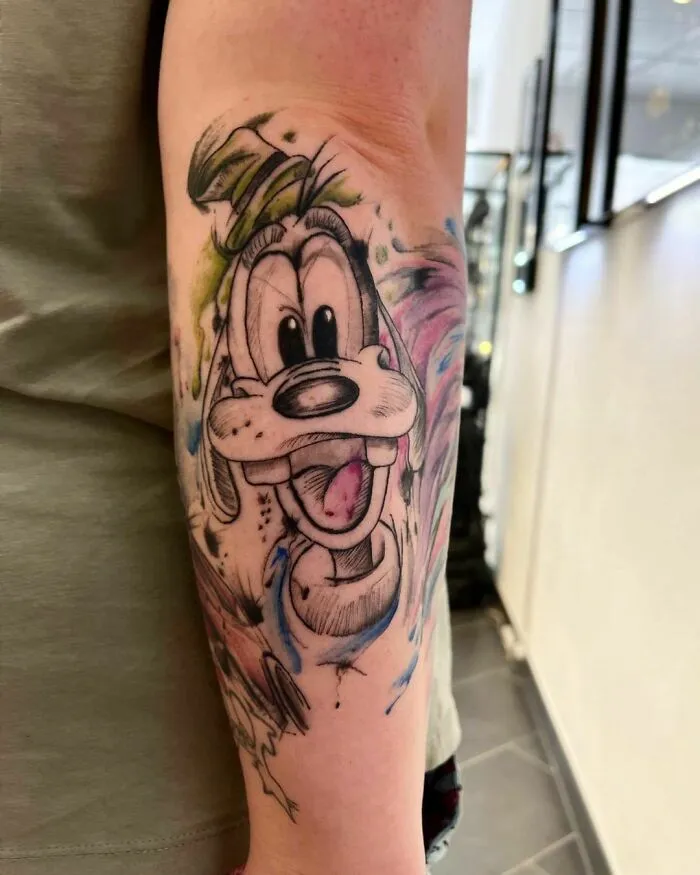 Cartoon tattoo of a happy dog character on forearm, inspired by favorite animated shows.