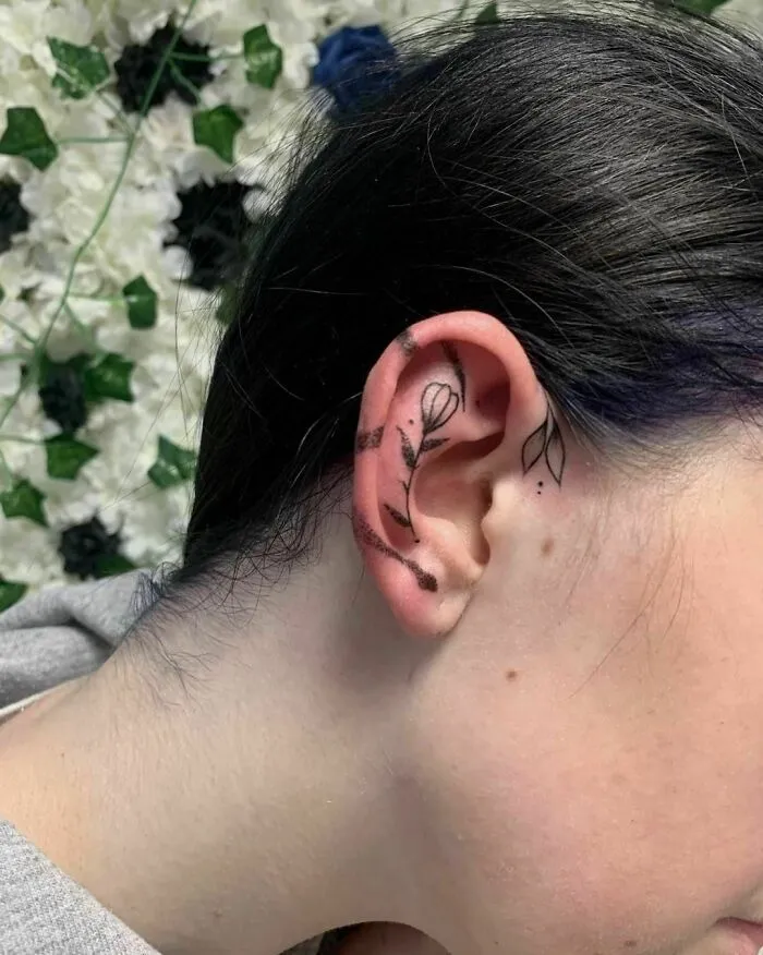 Delicate floral ear tattoo with leaves and petals behind a woman's ear.