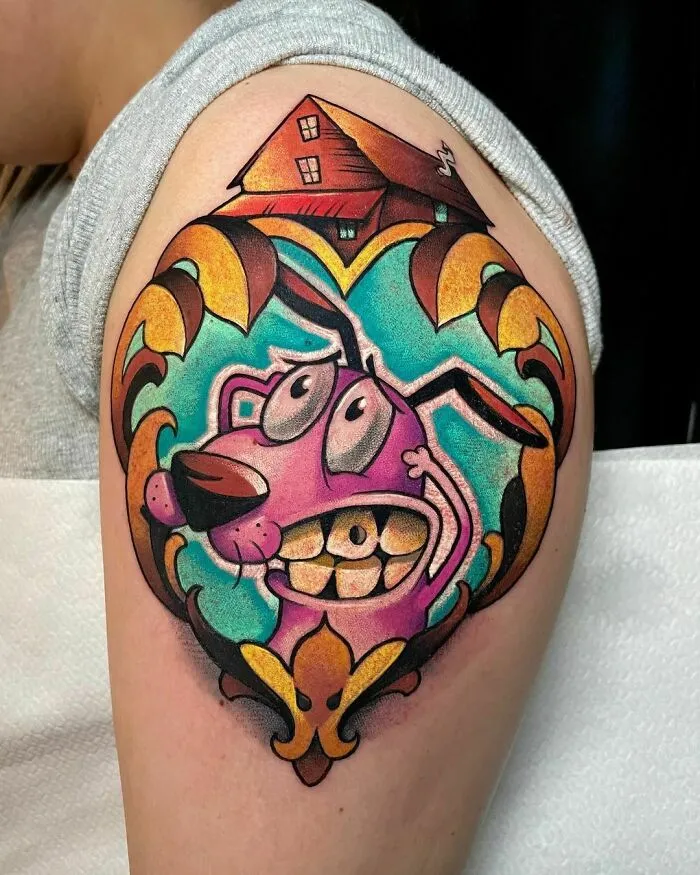 Cartoon tattoo of Courage the Cowardly Dog in a heart-shaped mirror, evoking nostalgia on upper arm.