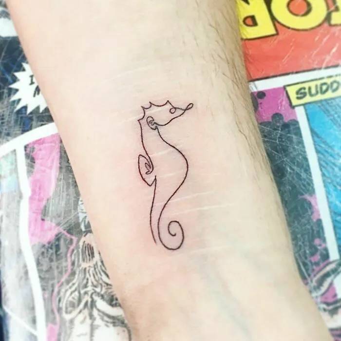 Fine-line seahorse tattoo on arm, showcasing single-line art on a comic background.