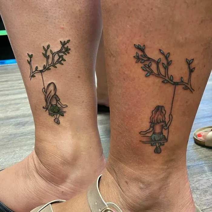 Matching best friend tattoos of girls on swings under leafy branches on ankles.
