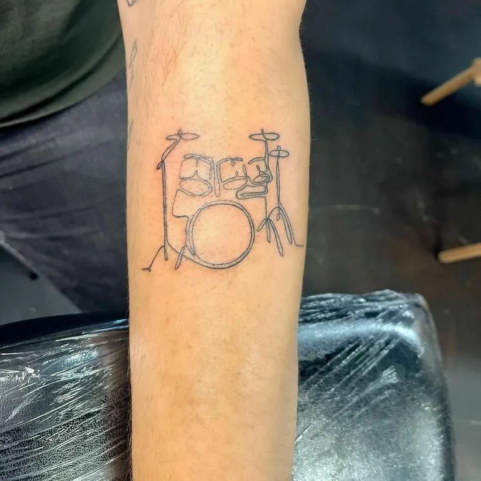Fine-line single-line tattoo of a drum set on an arm, showcasing minimalist design.