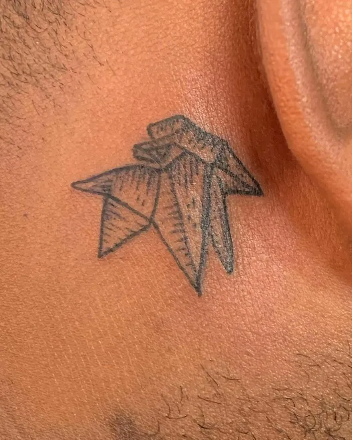 Origami-style ear tattoo on skin, featuring geometric shapes and fine line details.