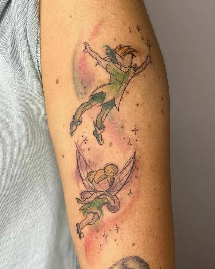 Cartoon tattoo of two flying characters from animated shows on an arm, with colorful background and stars.
