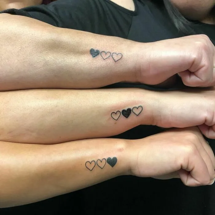 Three forearms with matching heart tattoos symbolizing friendship.