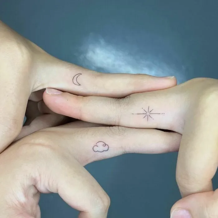 Minimalist best friend tattoos on fingers featuring a moon, star, and cloud design.
