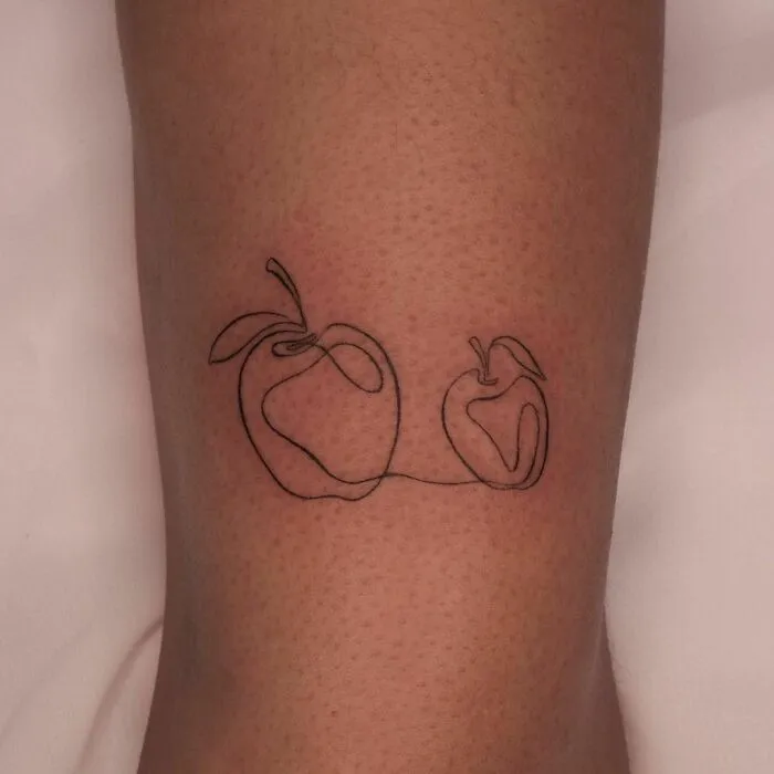 Single-line tattoo of two apples on skin, showcasing fine-line perfection.