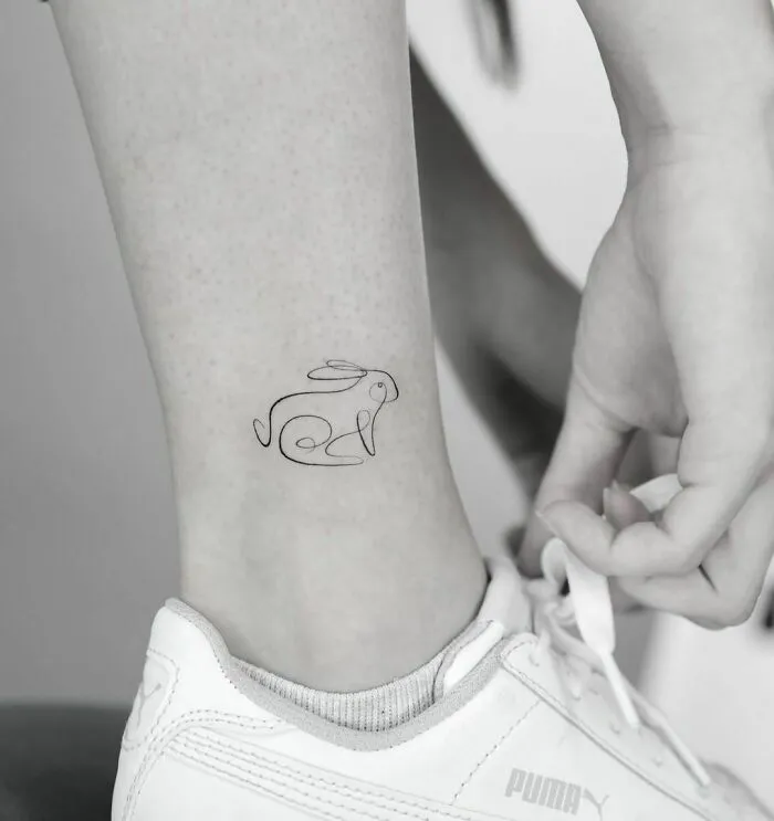 A single-line tattoo of a rabbit on an ankle, showcasing fine-line perfection.