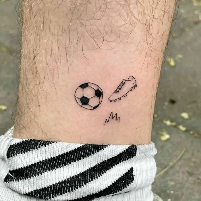 Minimalist tattoo of a soccer ball, cleat, and grass on a leg, emphasizing aesthetic appeal.
