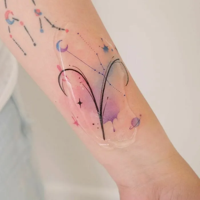 Watercolor tattoo featuring an abstract constellation design with soft pastel shades on a forearm.