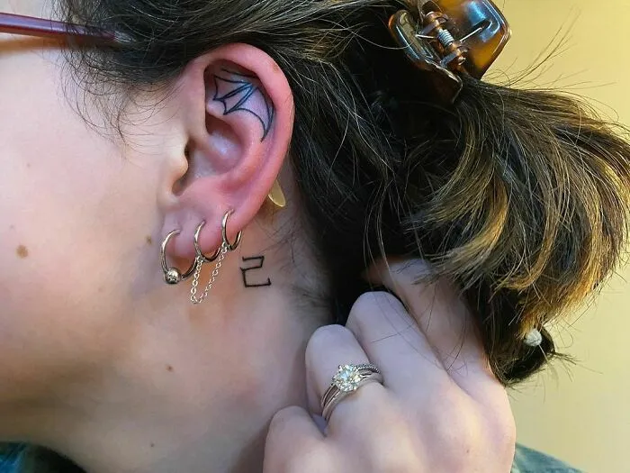 Ear tattoo with geometric design, multiple hoop earrings, and stylish hairstyle.