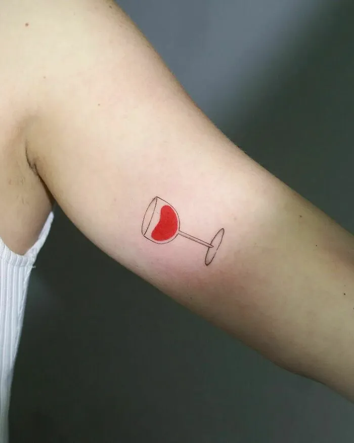 Minimalist tattoo of a wine glass with red contents on an arm, showcasing aesthetic design.