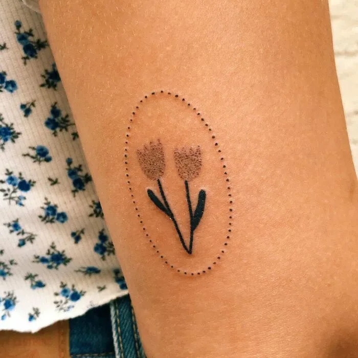 Minimalist tattoo of flowers outlined by dotted oval on arm.