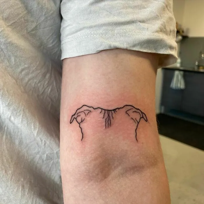 Minimalist tattoo of dog ears on an arm, highlighting aesthetics and simplicity.