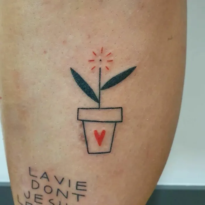 Minimalist tattoo of a potted plant with a heart on the pot, featuring simple lines and soft colors, on arm.
