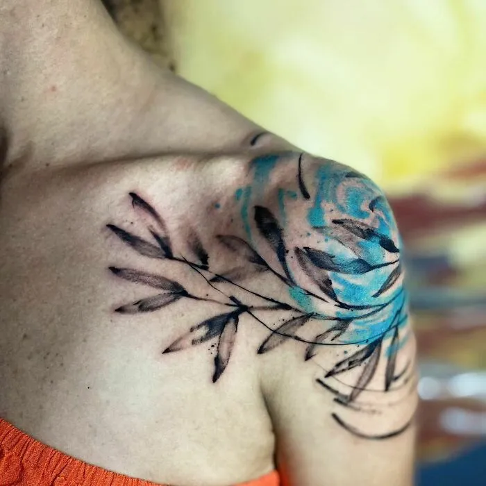 Watercolor tattoo on shoulder, featuring blue and black leaf design.