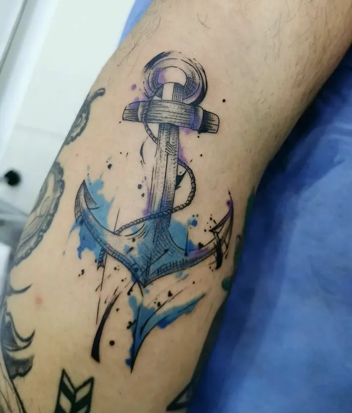 Watercolor tattoo of an anchor with blue splashes, showcasing a creative and artistic design.