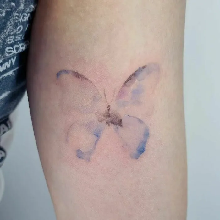 Watercolor tattoo of a butterfly on an arm, showcasing a soft, artistic design.