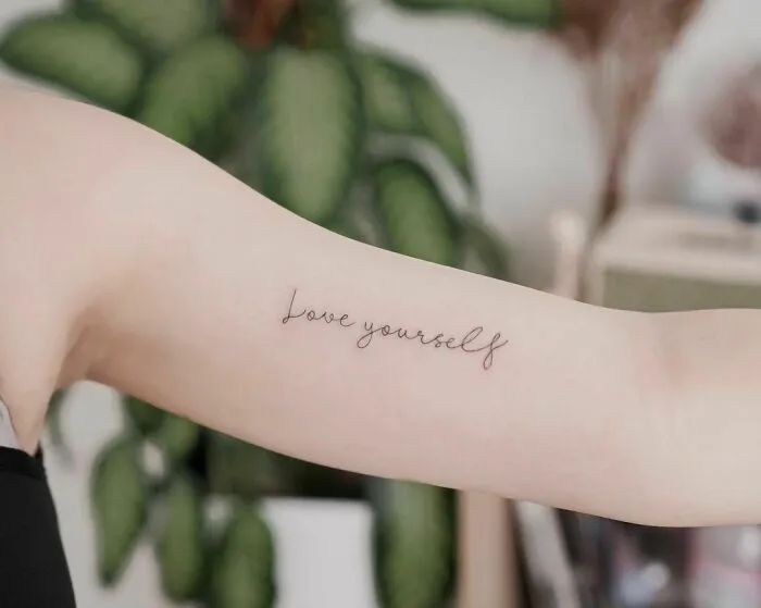 Arm with a "love yourself" word tattoo, simple and elegant design.
