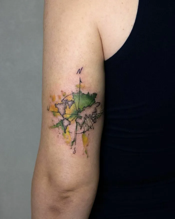 Watercolor tattoo of a world map with compass design on an upper arm, showcasing vibrant inkspiration.