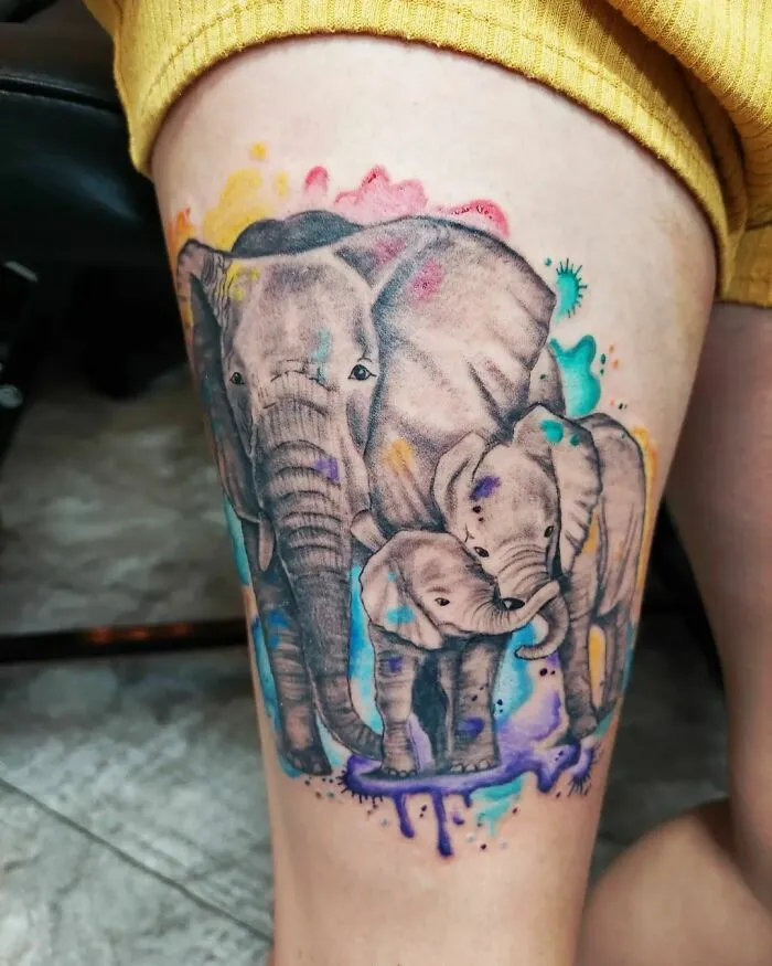 Watercolor tattoo of vibrant elephants on a thigh, showcasing artistic detail and vivid colors.