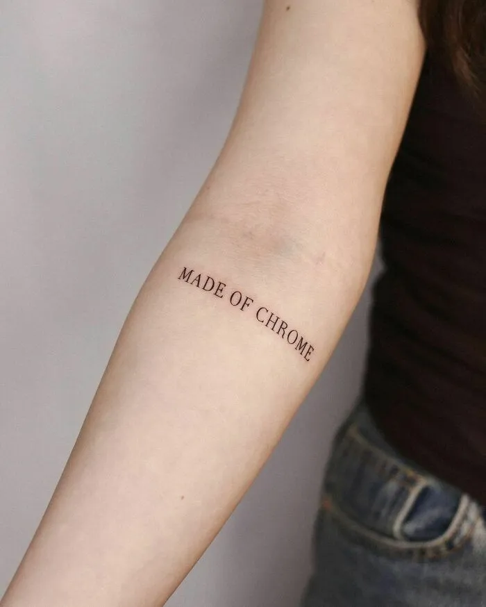 Close-up of an arm with a "MADE OF CHROME" word tattoo, related to meaningful word tattoos.