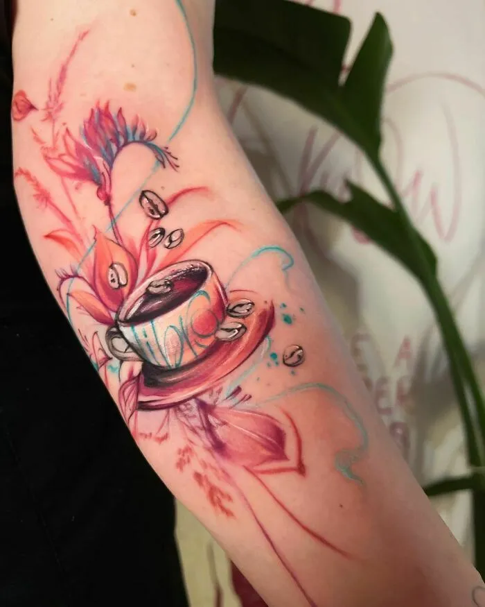 Watercolor tattoo of a coffee cup with abstract floral designs on an arm.