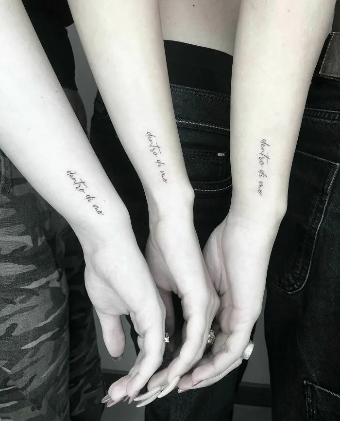 Three arms with word tattoos in cursive script, highlighting personal expressions through ink designs.
