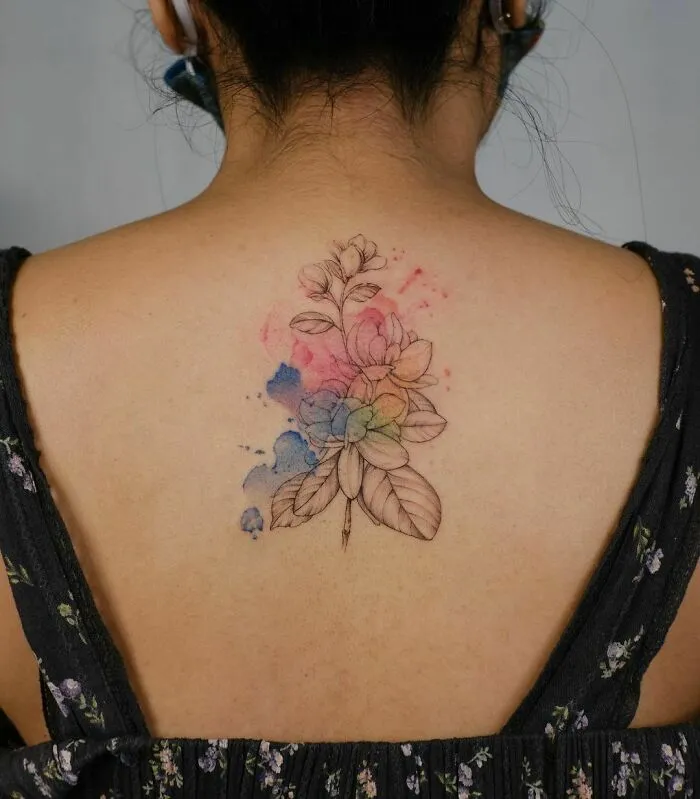 Watercolor tattoo of a floral design on a woman's back, featuring delicate colors and intricate details.