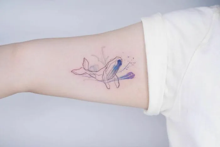 Delicate watercolor tattoo of a whale on an arm, showcasing beautiful minimalist art.